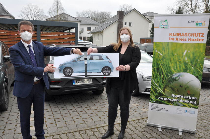 Landrat Michael Stickeln und Klimaschutzmanagerin Carolin Röttger halten gemeinsam ein Foto eines Autos in den Händen. Das Foto ist in der Mitte geteilt, was symbolisch für das 'Car-Sharing' stehen soll.