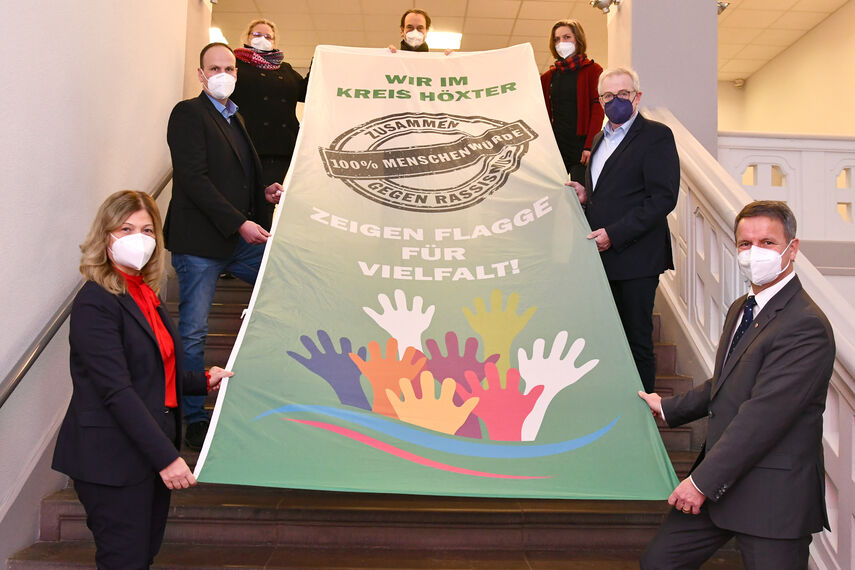 7 Personen halten einen Banner in der Hand mit der Aufschrift 'Flagge zeigen für Vielfalt'.