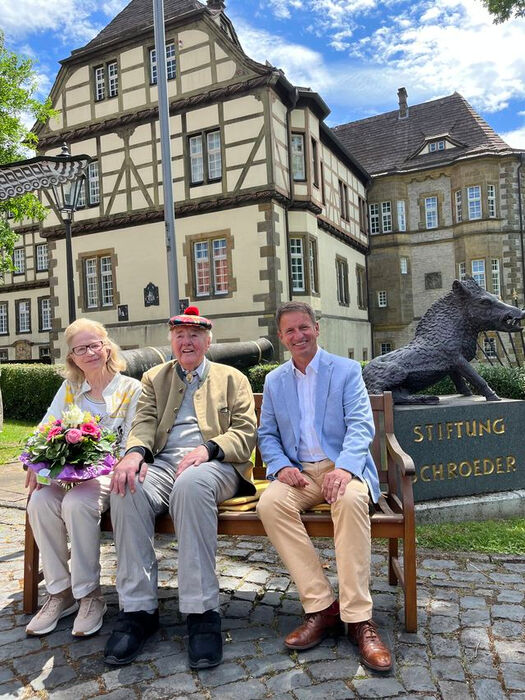 Ehepaar Schröder und Landrat Michael Stickeln sitzen auf einer Bank vor dem Wasserschloss in Neuenheerse.